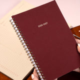 Maroon planner with 2026-2027 text held by a hand on a light background