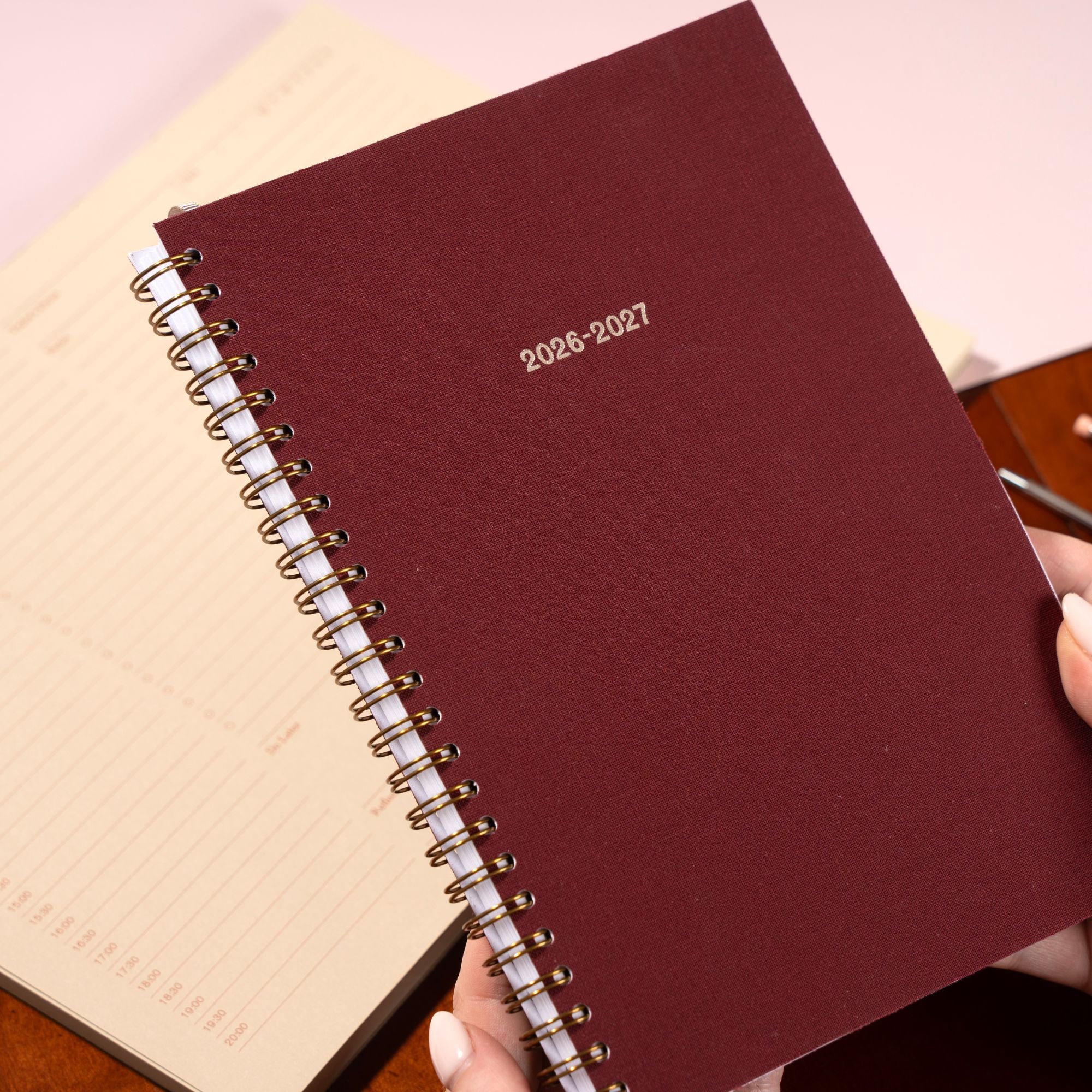 Maroon planner with 2026-2027 text held by a hand on a light background