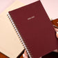 Maroon planner with 2026-2027 text held by a hand on a light background