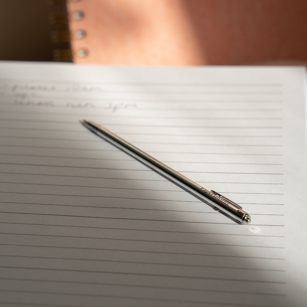 Silver pocket pen lying on ruled notebook by Papersmiths