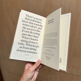 Open book with text held by a hand against a wooden background