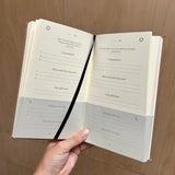 Open book with daily reflection pages held by a hand on a wooden surface