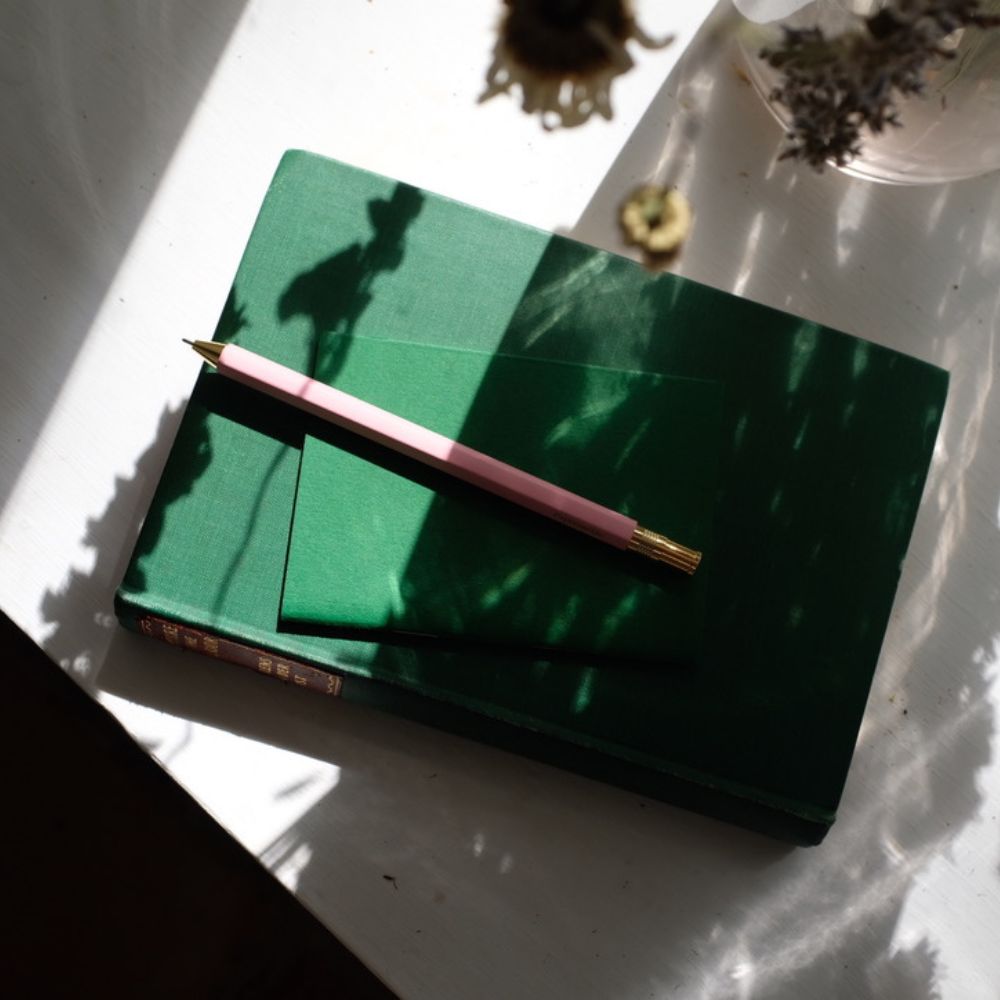 Green notebook with a pink pen on a white surface
