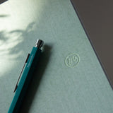 Blue pen on a green surface with a logo, on a blurred natural background