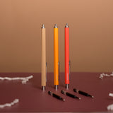 Three pens in beige, orange, and red on a brown surface with a brown background