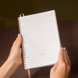 Person holding a spiral-bound planner with lined pages against a dark background
