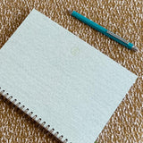 Light blue notebook with a green logo on a textured brown surface, accompanied by a blue pen.