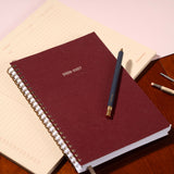 Maroon planner with a pen on a wooden surface