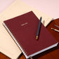 Maroon planner with a pen on a wooden surface