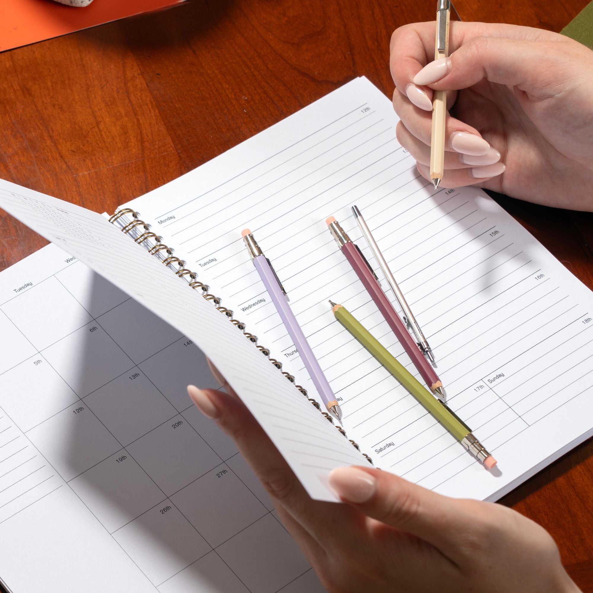 Person holding a pen over an open planner with other pens on the page.