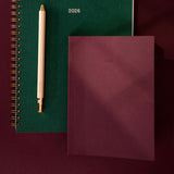 Green planner with a pen and burgundy notebook on a dark background