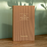 Brown journal titled 'The Five Minute Journal' by Papersmiths on a wooden surface with a blurred green background