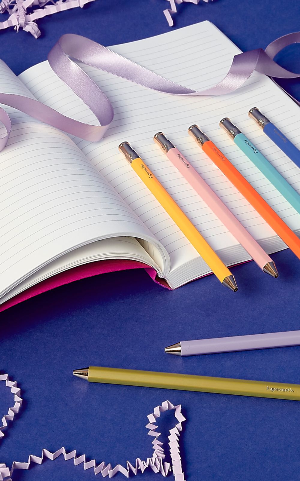 Colorful pens on an open notebook with ribbons on a blue background