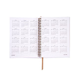 Open spiral-bound planner with calendar pages on a white background