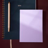 lavender planner with a pencil and blue notebook on a gradient background