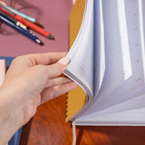 Hand holding an open notebook with pens in the background