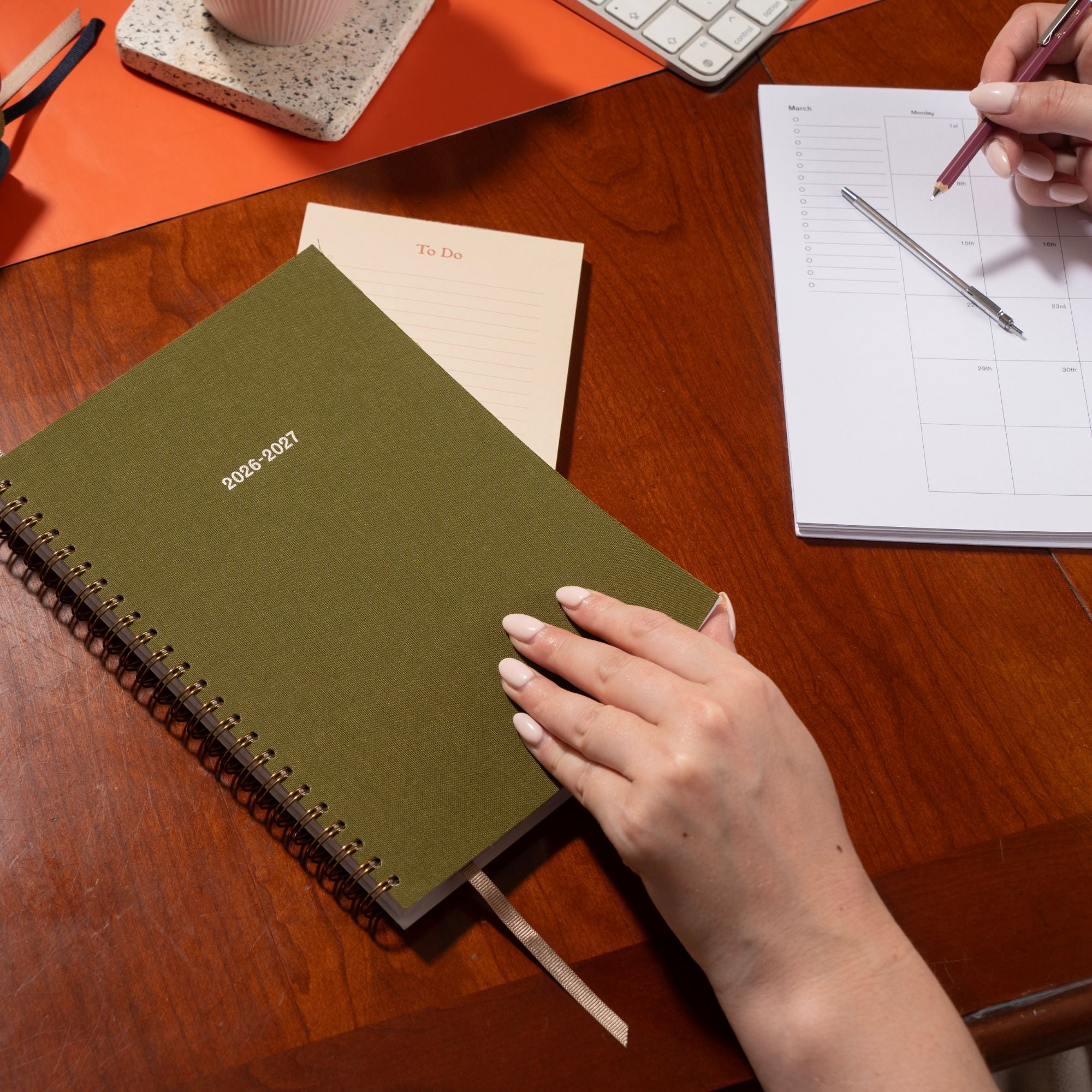Person holding a green planner on a desk with office supplies.