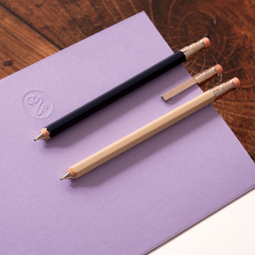 Three pocket pencils on a purple notebook with a wooden surface underneath