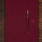 Maroon notebook with a matching pocket pencil on a wooden surface