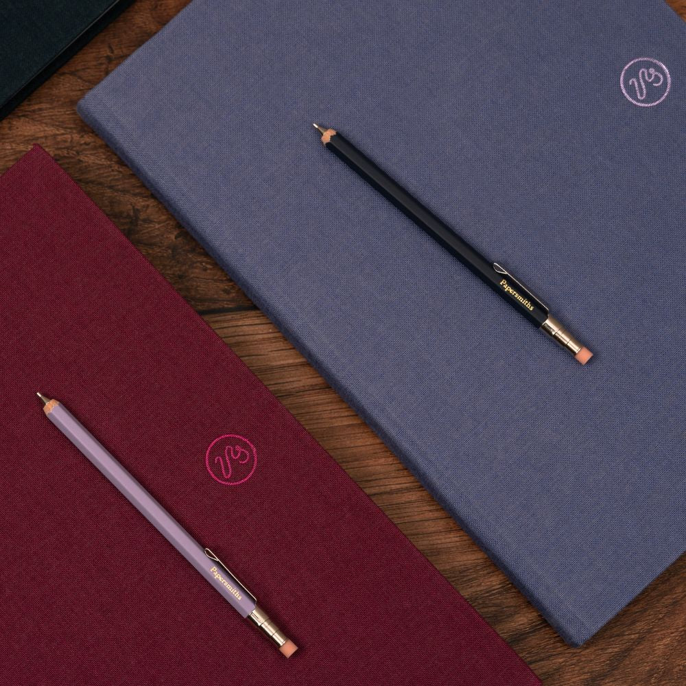 Two notebooks, one red and one blue, with two pencils on a wooden surface.