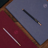 Two notebooks, one red and one blue, with two pencils on a wooden surface.
