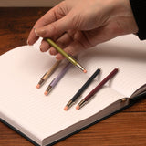 Hand holding a pencil over an open book with other pencils on the page.