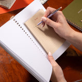 Person writing in a notebook with a pen on a wooden surface