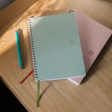 Two spiral-bound notebooks on a wooden surface with a pen next to them.